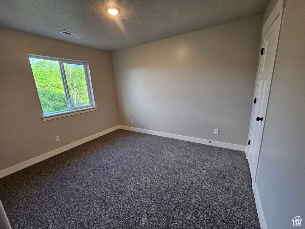 Unfurnished room with baseboards, dark carpet, and a textured ceiling