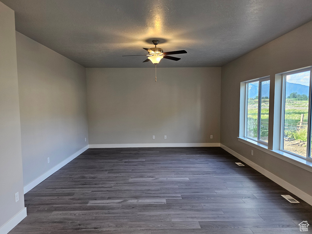 Empty room featuring a ceiling fan, a textured ceiling, dark wood-type flooring, and baseboards