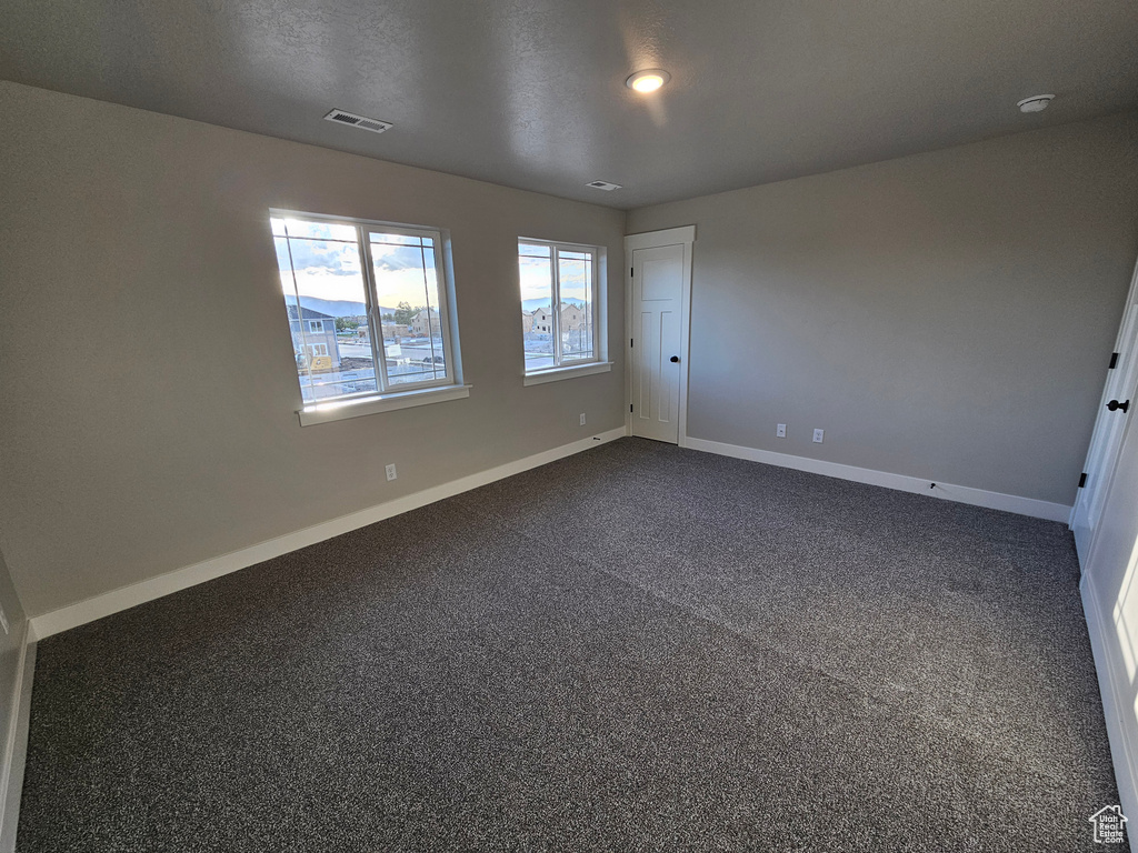 Unfurnished room featuring baseboards, dark carpet, and a smoke detector