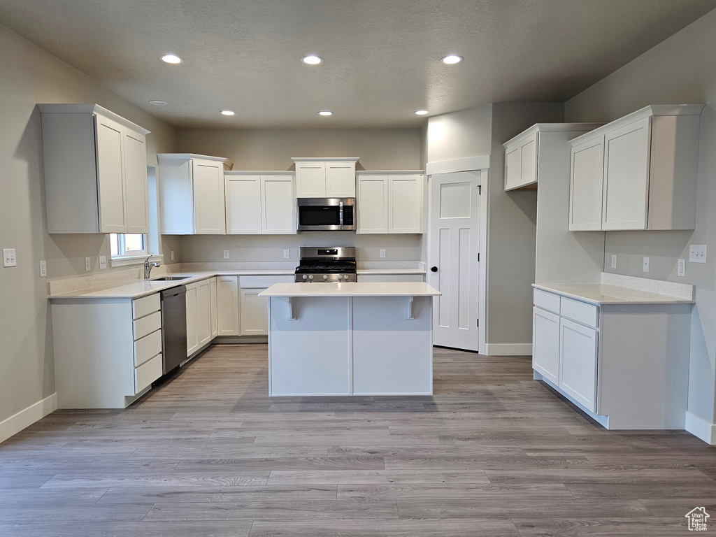 Kitchen with appliances with stainless steel finishes, baseboards, a kitchen island, recessed lighting, and white cabinetry