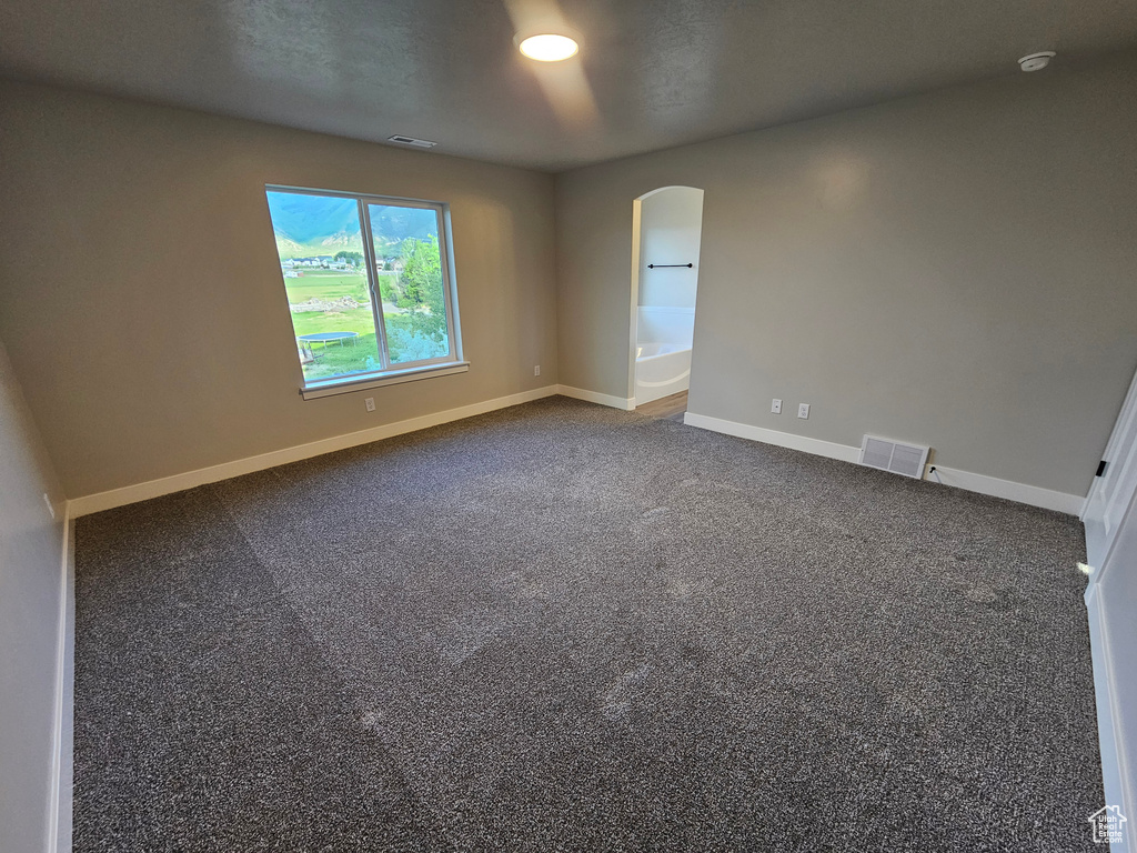 Spare room featuring arched walkways, baseboards, dark carpet, and a smoke detector