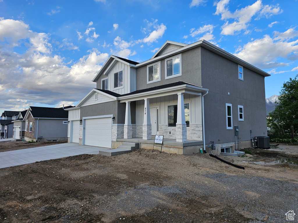 View of front facade featuring a porch, driveway, board and batten siding, stone siding, and central AC