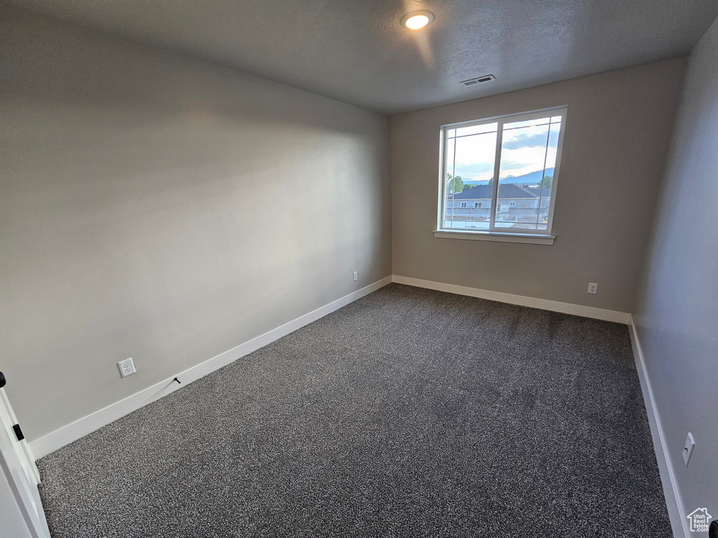 Empty room featuring dark carpet and baseboards
