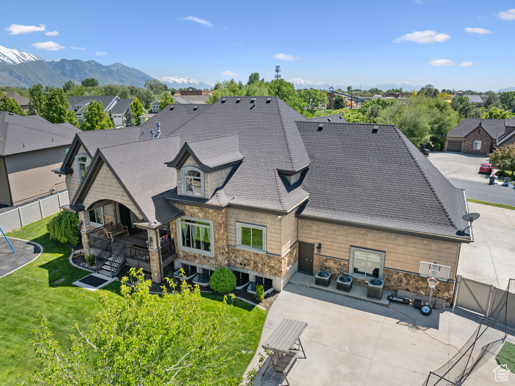 Rear view of property featuring a patio area, stone siding, roof with shingles, a residential view, and a mountain view