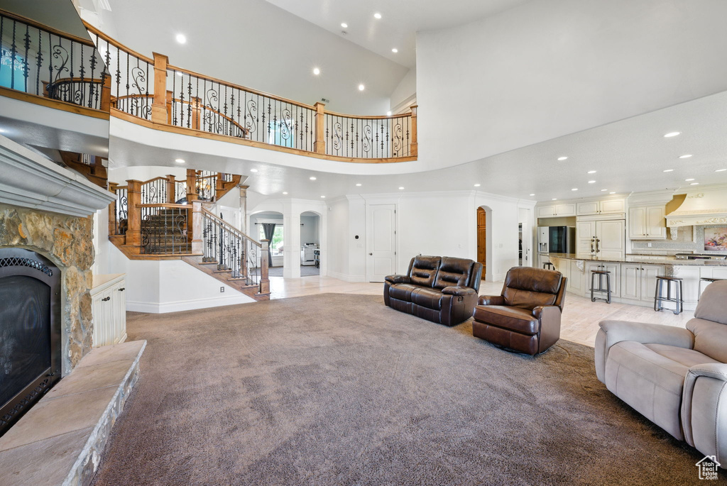 Living area with recessed lighting, a towering ceiling, stairs, arched walkways, and a stone fireplace