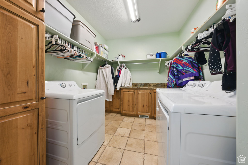 Laundry area with separate washer and dryer, cabinet space, and light tile patterned floors