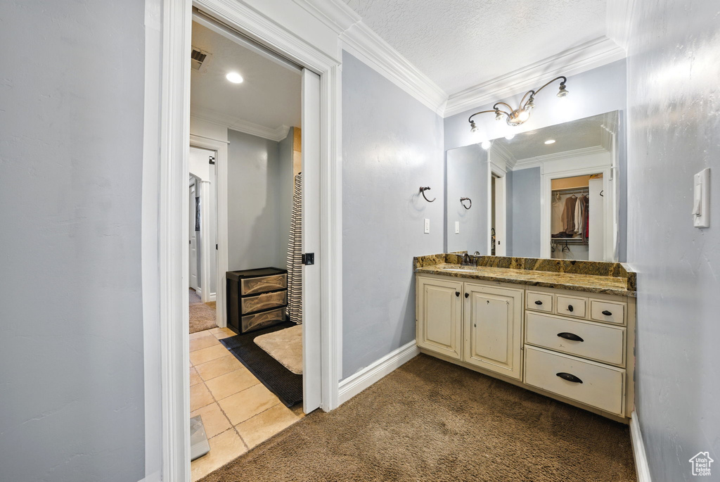 Full bath with crown molding, vanity, a spacious closet, tile patterned flooring, and baseboards