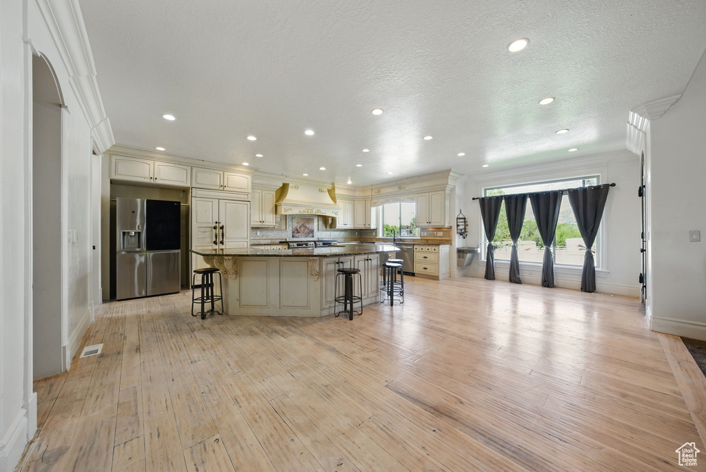 Kitchen with stainless steel refrigerator with ice dispenser, a breakfast bar, cream cabinets, light wood-style flooring, and ornamental molding