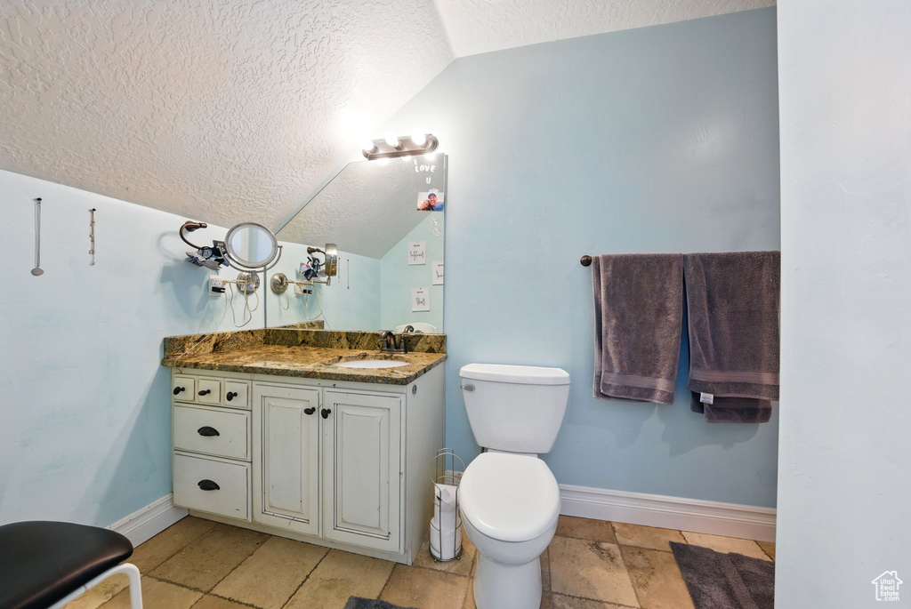Bathroom with vaulted ceiling, a textured ceiling, baseboards, vanity, and toilet