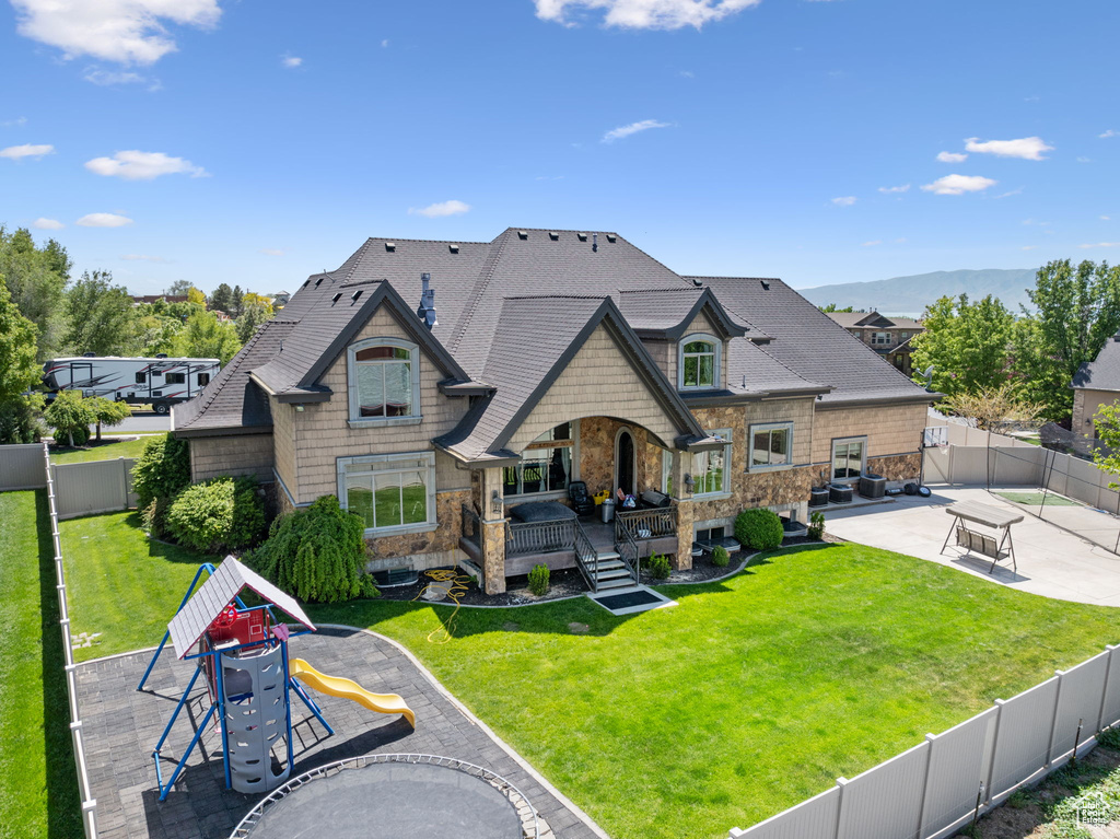 Back of property featuring stone siding, a patio area, a deck, and a shingled roof