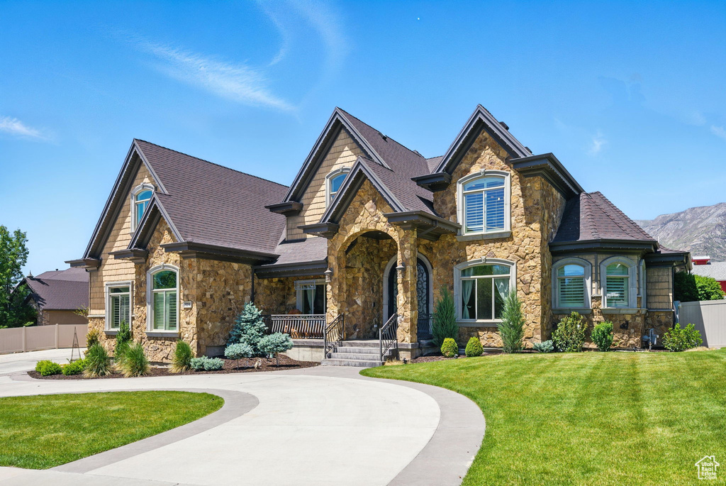 View of front of property featuring stone siding, a porch, roof with shingles, and curved driveway