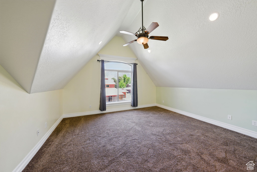 Additional living space with a ceiling fan, carpet, baseboards, lofted ceiling, and a textured ceiling