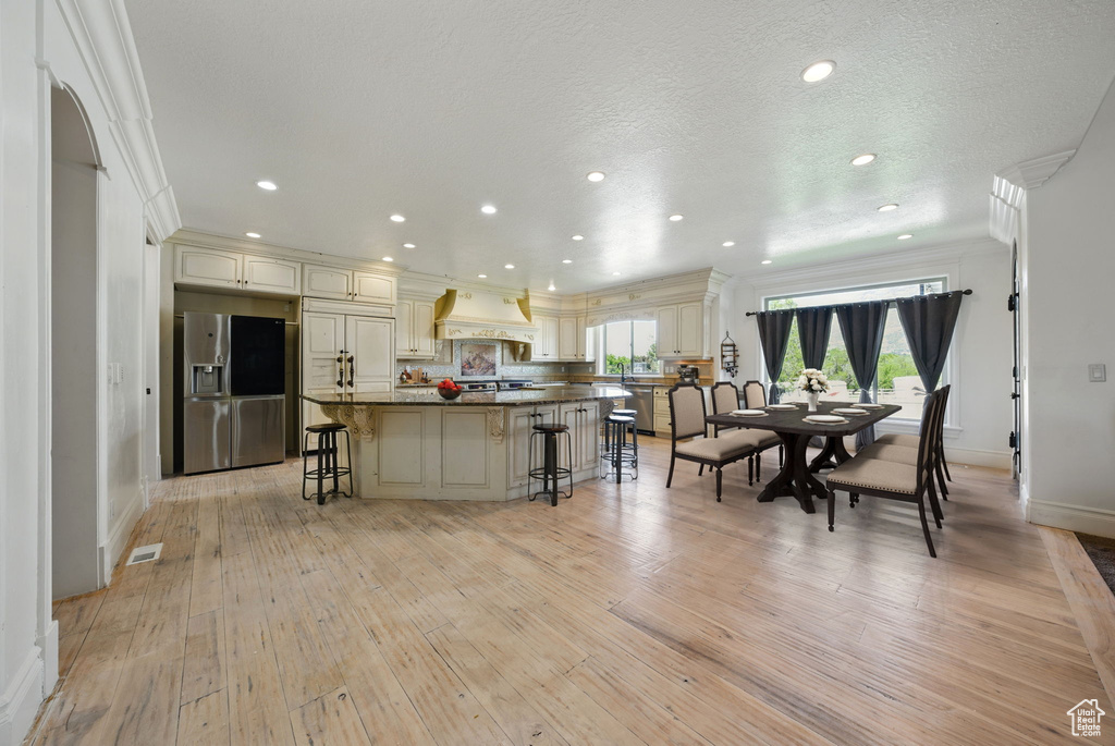 Kitchen with stainless steel fridge with ice dispenser, a breakfast bar, cream cabinets, baseboards, and ornamental molding