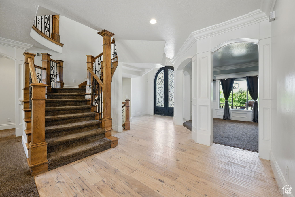 Entrance foyer with decorative columns, arched walkways, light wood-style floors, stairway, and ornamental molding