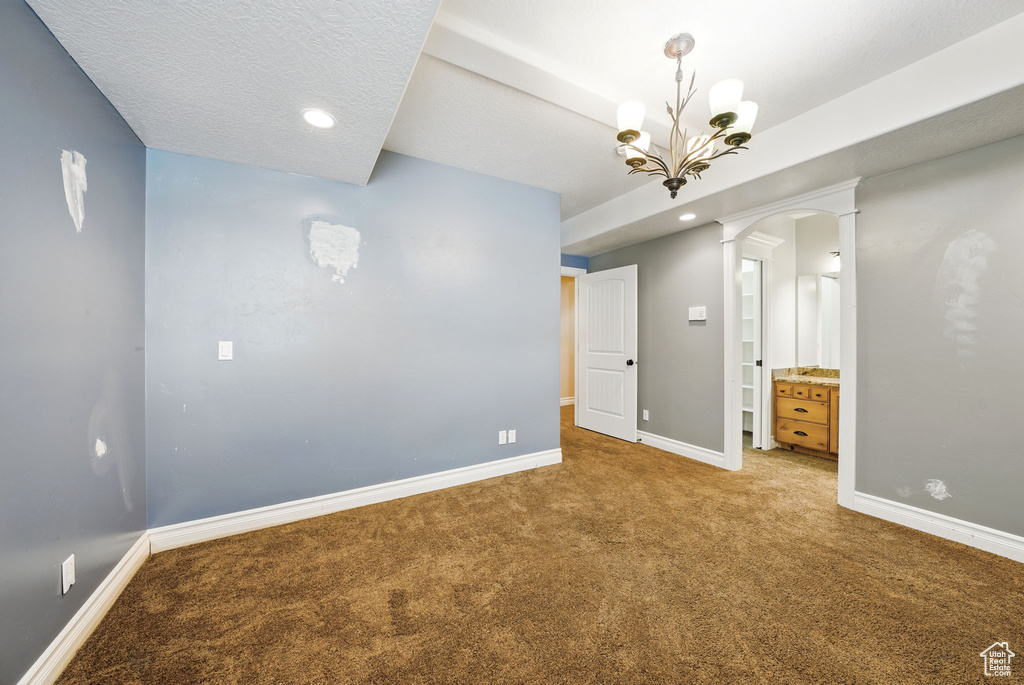 Carpeted empty room featuring ornate columns, baseboards, a chandelier, recessed lighting, and arched walkways