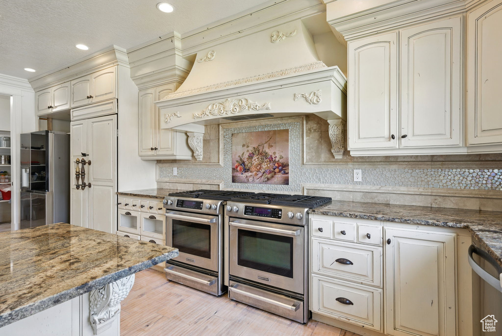 Kitchen featuring appliances with stainless steel finishes, cream cabinets, premium range hood, decorative backsplash, and recessed lighting