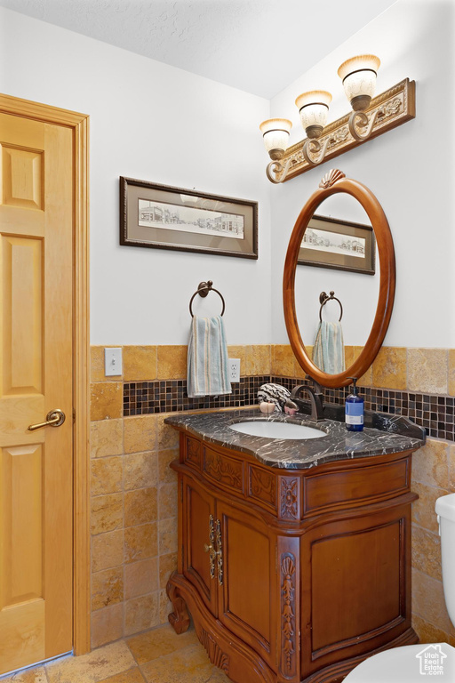 Half bathroom with tile walls, vanity, wainscoting, and toilet