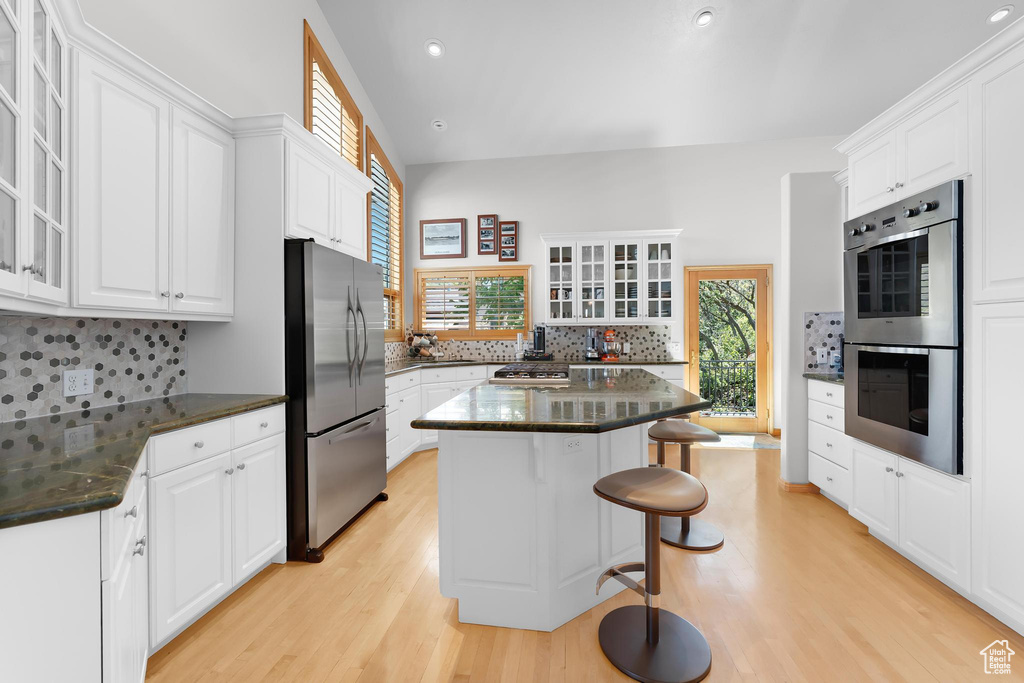 Kitchen with appliances with stainless steel finishes, light wood-style floors, a breakfast bar area, white cabinetry, and recessed lighting