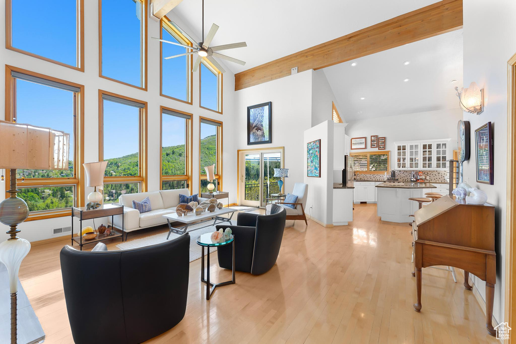 Living room featuring high vaulted ceiling, plenty of natural light, beamed ceiling, light wood-type flooring, and a ceiling fan