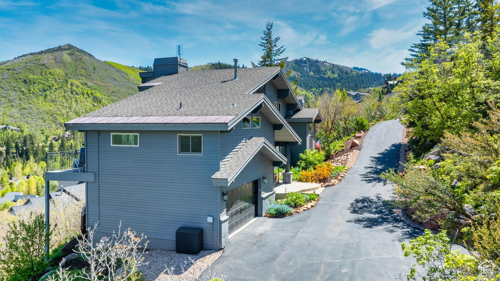 View of side of property featuring a mountain view, asphalt driveway, a chimney, and a shingled roof