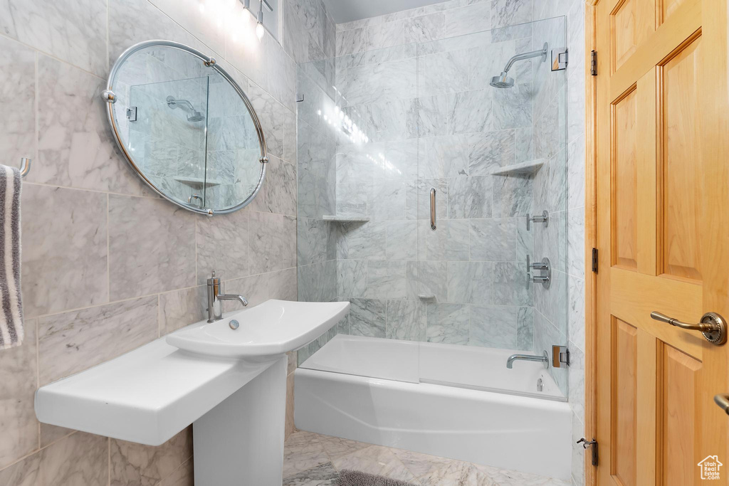Full bathroom featuring shower / bath combination with glass door, tile walls, and a sink