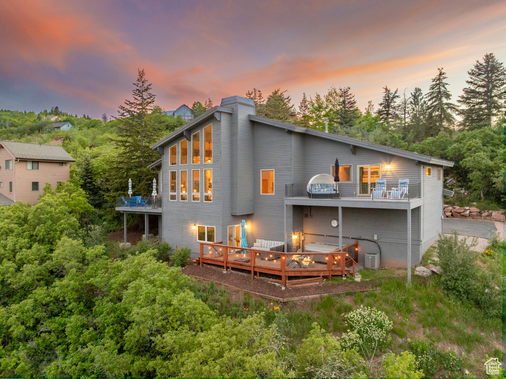 Rear view of property featuring a wooden deck, a chimney, view of wooded area, and a balcony