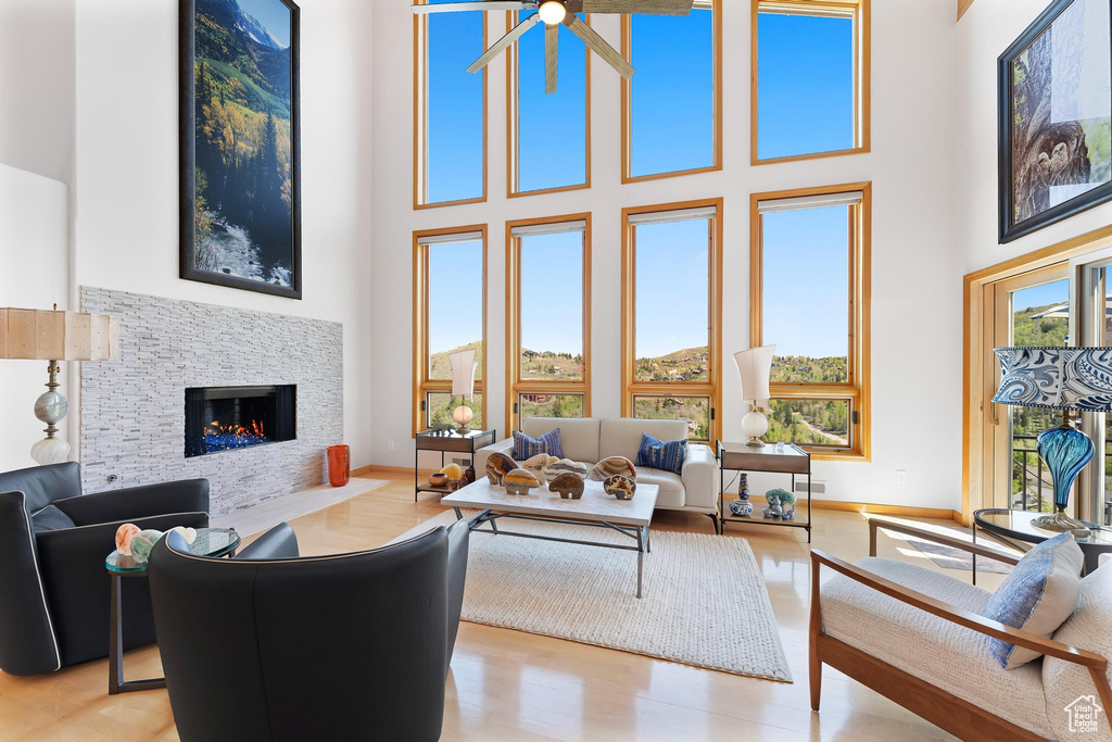 Living room featuring a towering ceiling, a warm lit fireplace, baseboards, and wood finished floors
