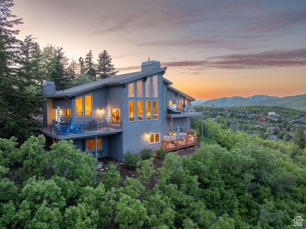 Back of house at dusk featuring a chimney, a balcony, and a mountain view