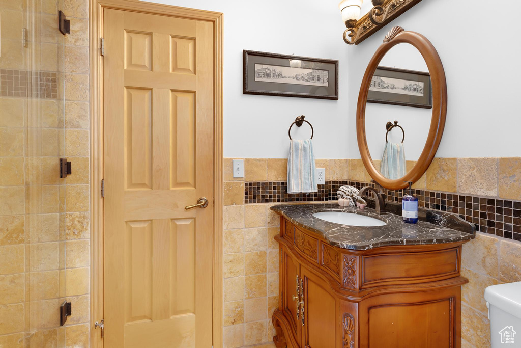 Full bath with tile walls, vanity, toilet, wainscoting, and tiled shower