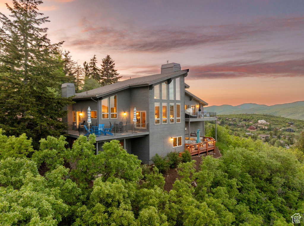 Back of property at dusk with a chimney, a balcony, and a deck with mountain view