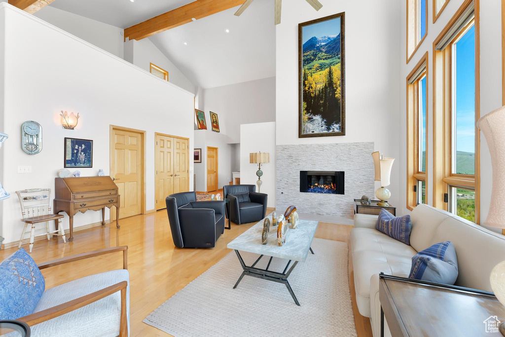 Living room with high vaulted ceiling, light wood-style flooring, beamed ceiling, a glass covered fireplace, and a ceiling fan