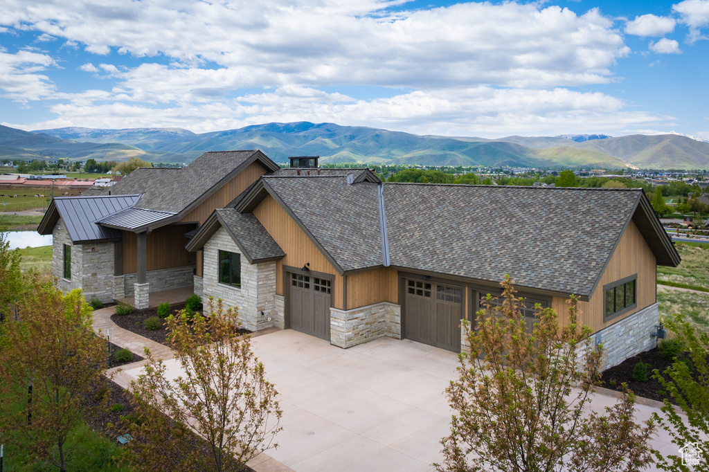 View of front of property with stone siding, an attached garage, a mountain view, driveway, and a standing seam roof