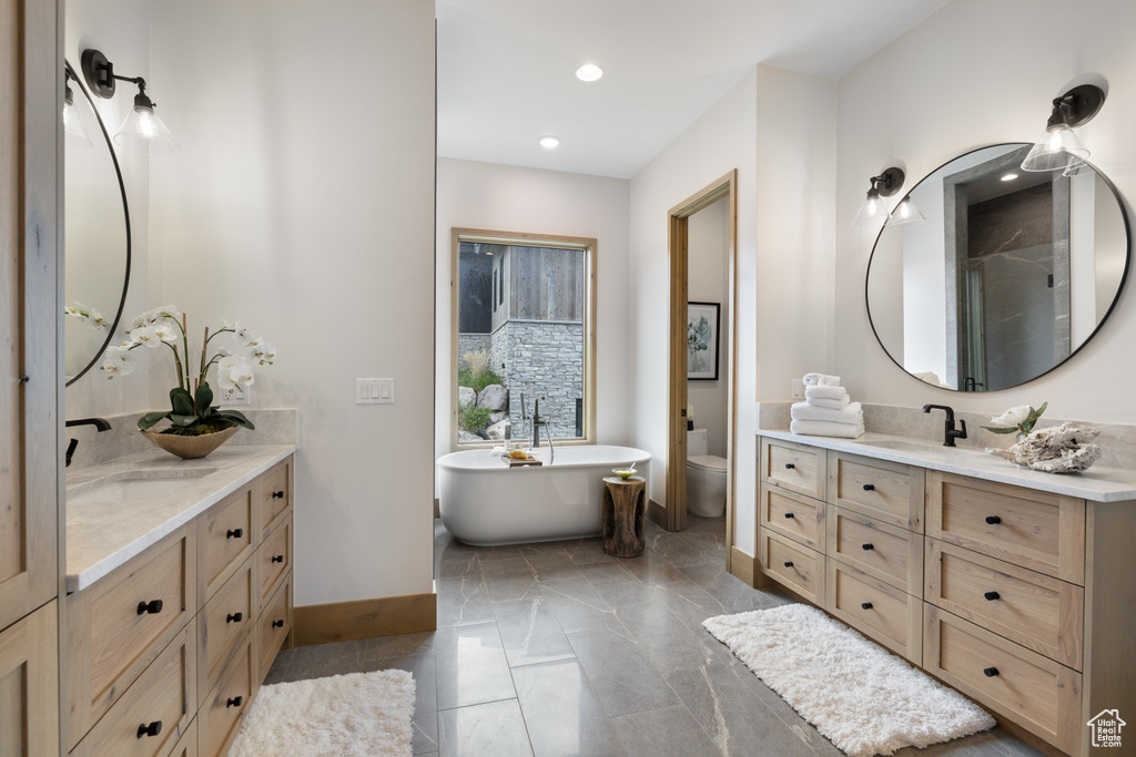 Full bathroom with baseboards, vanity, toilet, a freestanding bath, and a stall shower
