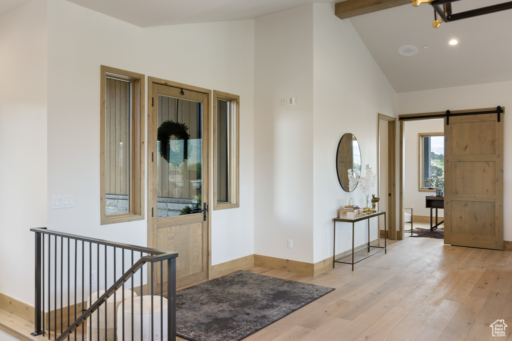 Foyer entrance with a barn door, baseboards, high vaulted ceiling, light wood finished floors, and beamed ceiling