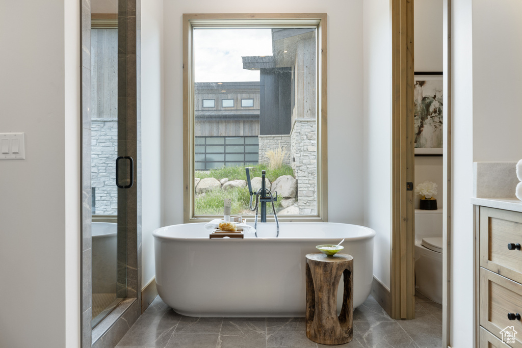Bathroom featuring a freestanding bath, toilet, marble finish flooring, and a shower stall
