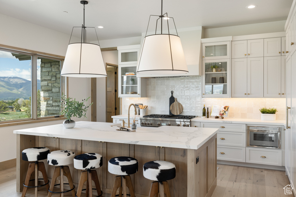 Kitchen featuring backsplash, a breakfast bar, light wood-type flooring, white cabinetry, and recessed lighting
