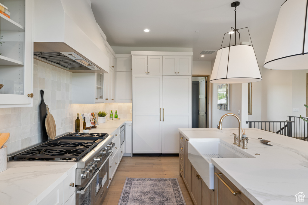 Kitchen featuring custom range hood, a sink, light wood-style flooring, white cabinetry, and recessed lighting