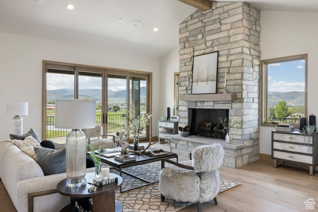 Living area featuring a mountain view, light wood finished floors, a stone fireplace, beam ceiling, and high vaulted ceiling