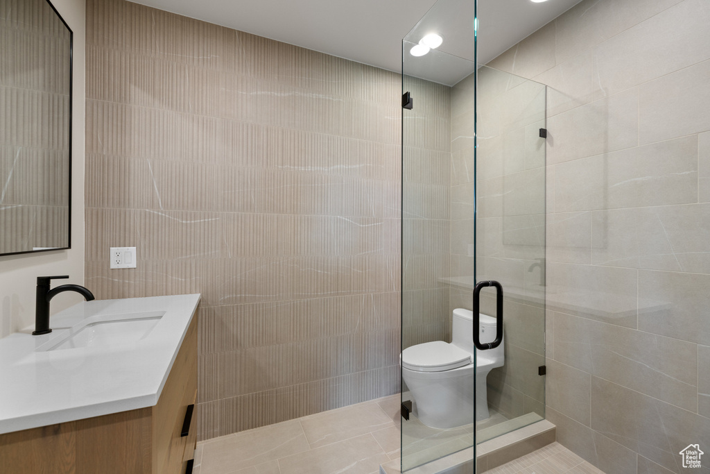 Bathroom featuring tile walls, toilet, vanity, tiled shower, and tile patterned flooring