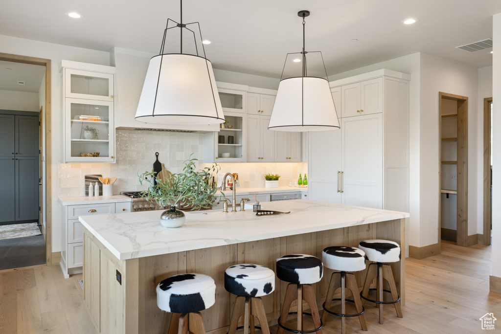 Kitchen with light wood finished floors, recessed lighting, a center island with sink, a kitchen breakfast bar, and light stone counters