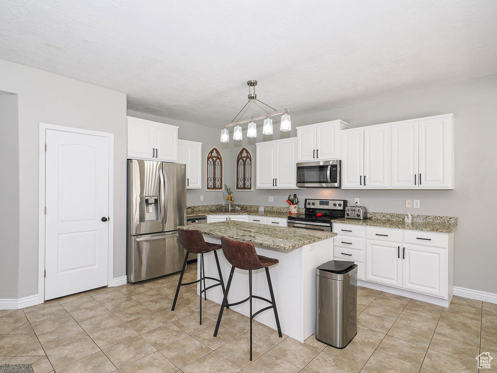 Kitchen featuring stainless steel appliances, a breakfast bar, white cabinetry, a center island, and baseboards