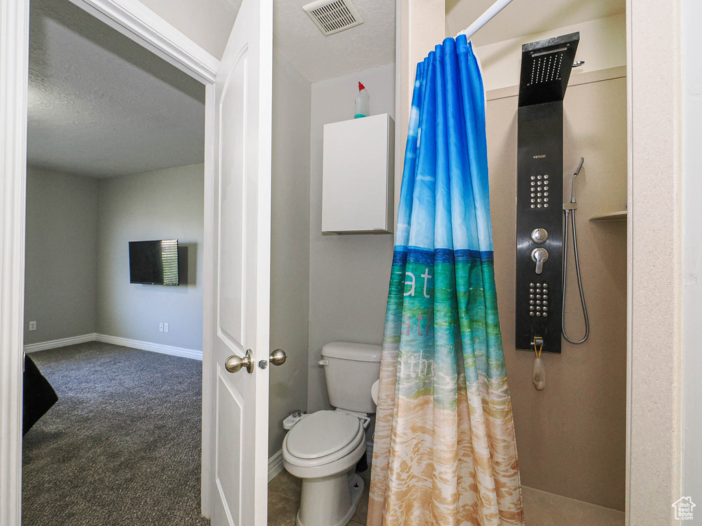 Bathroom featuring a shower with curtain, toilet, baseboards, and a textured ceiling