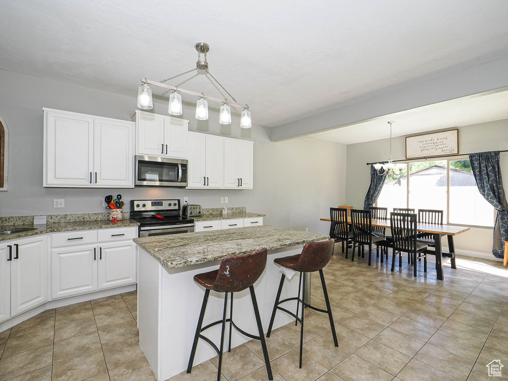 Kitchen featuring appliances with stainless steel finishes, light stone countertops, a kitchen island, and white cabinets