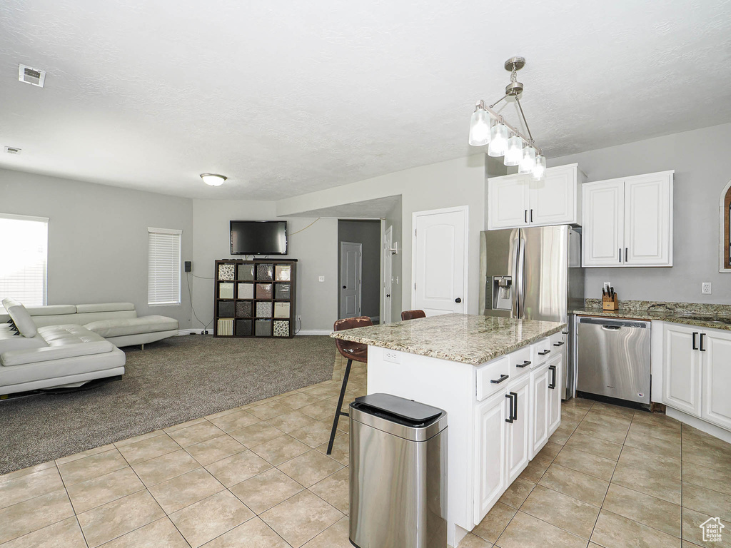 Kitchen with appliances with stainless steel finishes, light colored carpet, light tile patterned flooring, and white cabinetry
