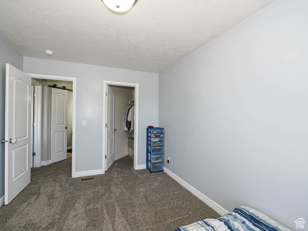 Unfurnished bedroom with dark carpet, a textured ceiling, and baseboards