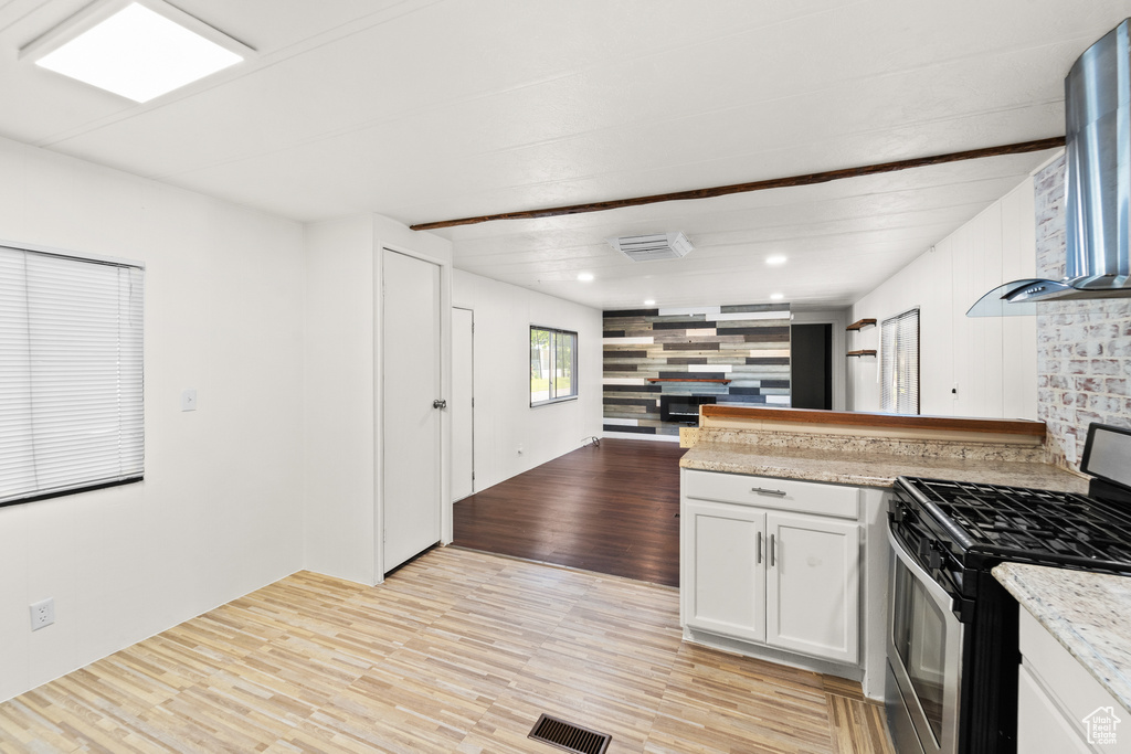 Kitchen with stainless steel range with gas stovetop, light wood-style flooring, a peninsula, open floor plan, and white cabinets