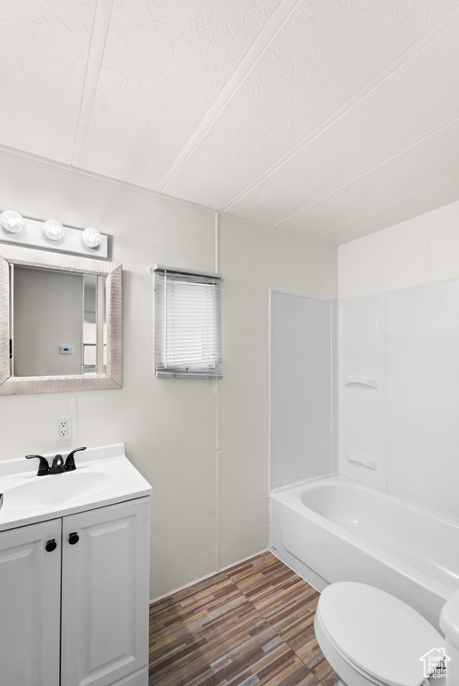 Bathroom featuring toilet, vanity, wood finished floors, a textured ceiling, and washtub / shower combination
