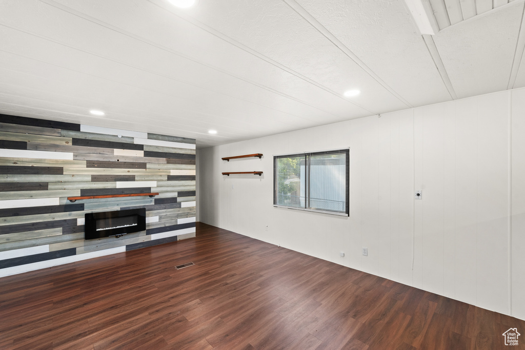 Unfurnished living room with wood finished floors, a glass covered fireplace, recessed lighting, and wood walls