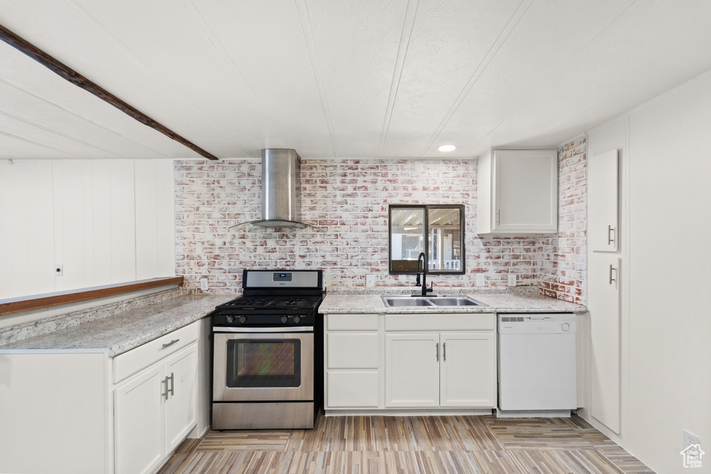 Kitchen with white dishwasher, wall chimney exhaust hood, a sink, gas stove, and white cabinets