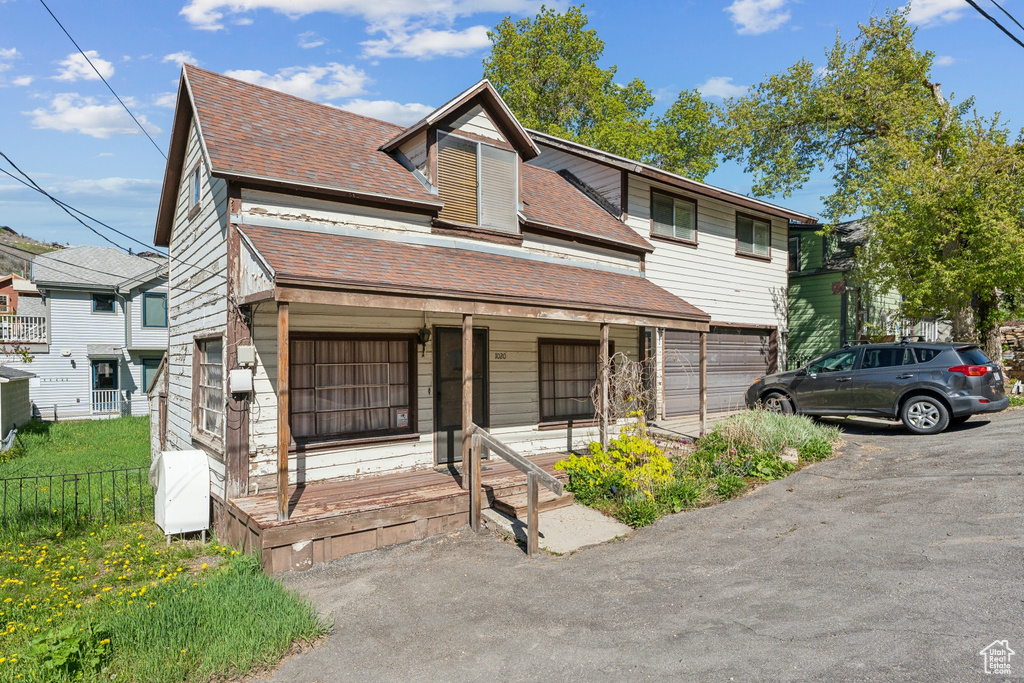 View of front facade featuring a porch, roof with shingles, and driveway